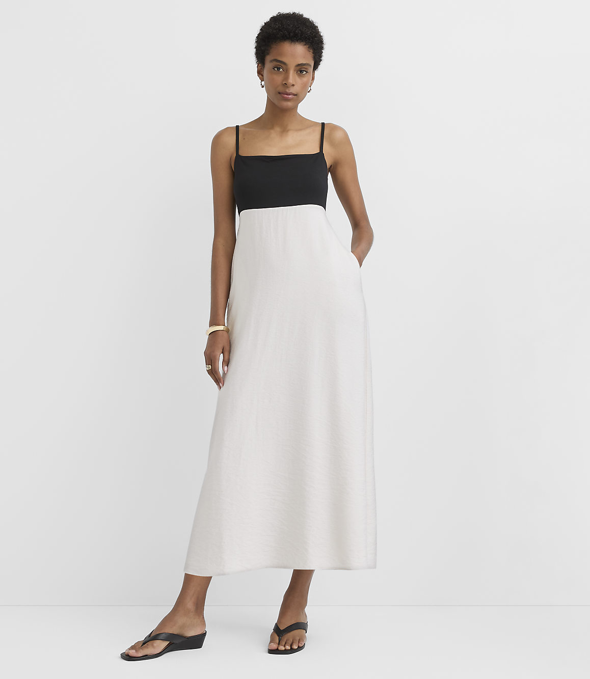 A woman in a black and white maxi dress stands with her hands in her pockets against a plain white background.
