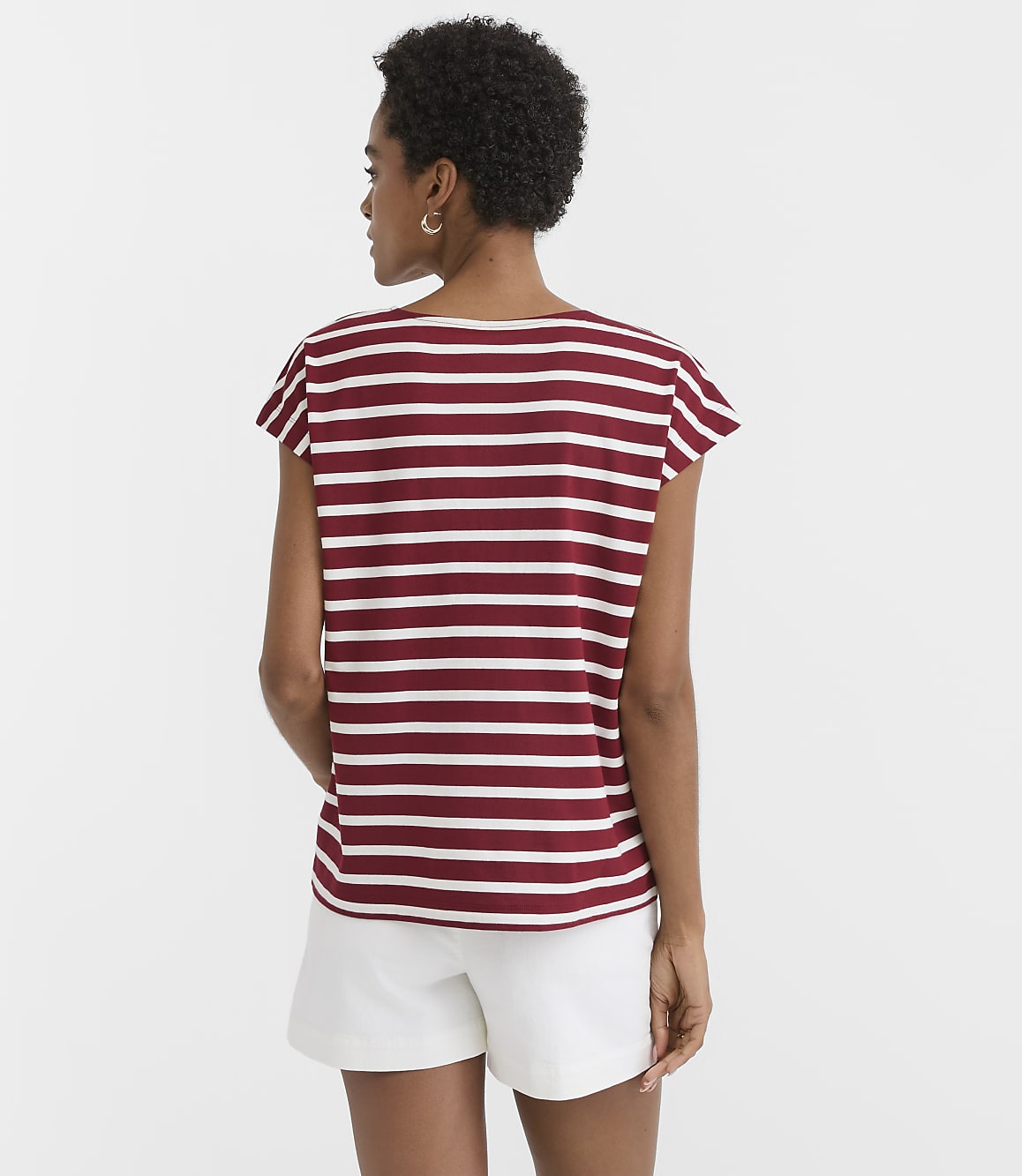 A woman in a striped shirt and white shorts stands against a plain white background.