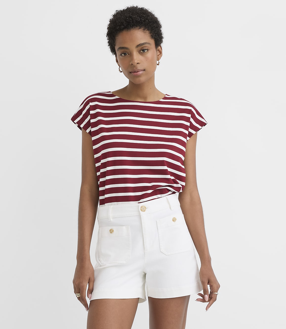 A woman in a striped t-shirt and white shorts stands against a plain white background.