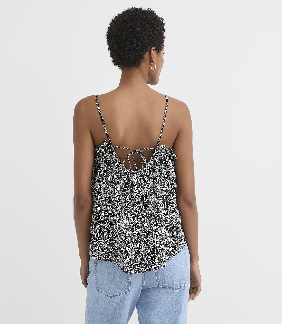 A woman in a patterned camisole and jeans stands against a plain white background.