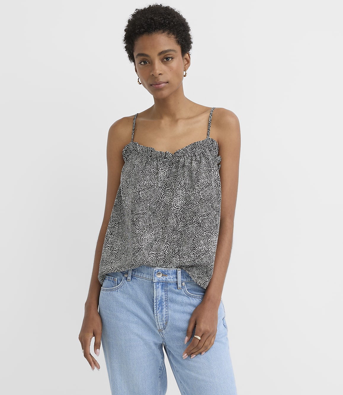A woman in a patterned camisole and light blue jeans stands against a plain white background.
