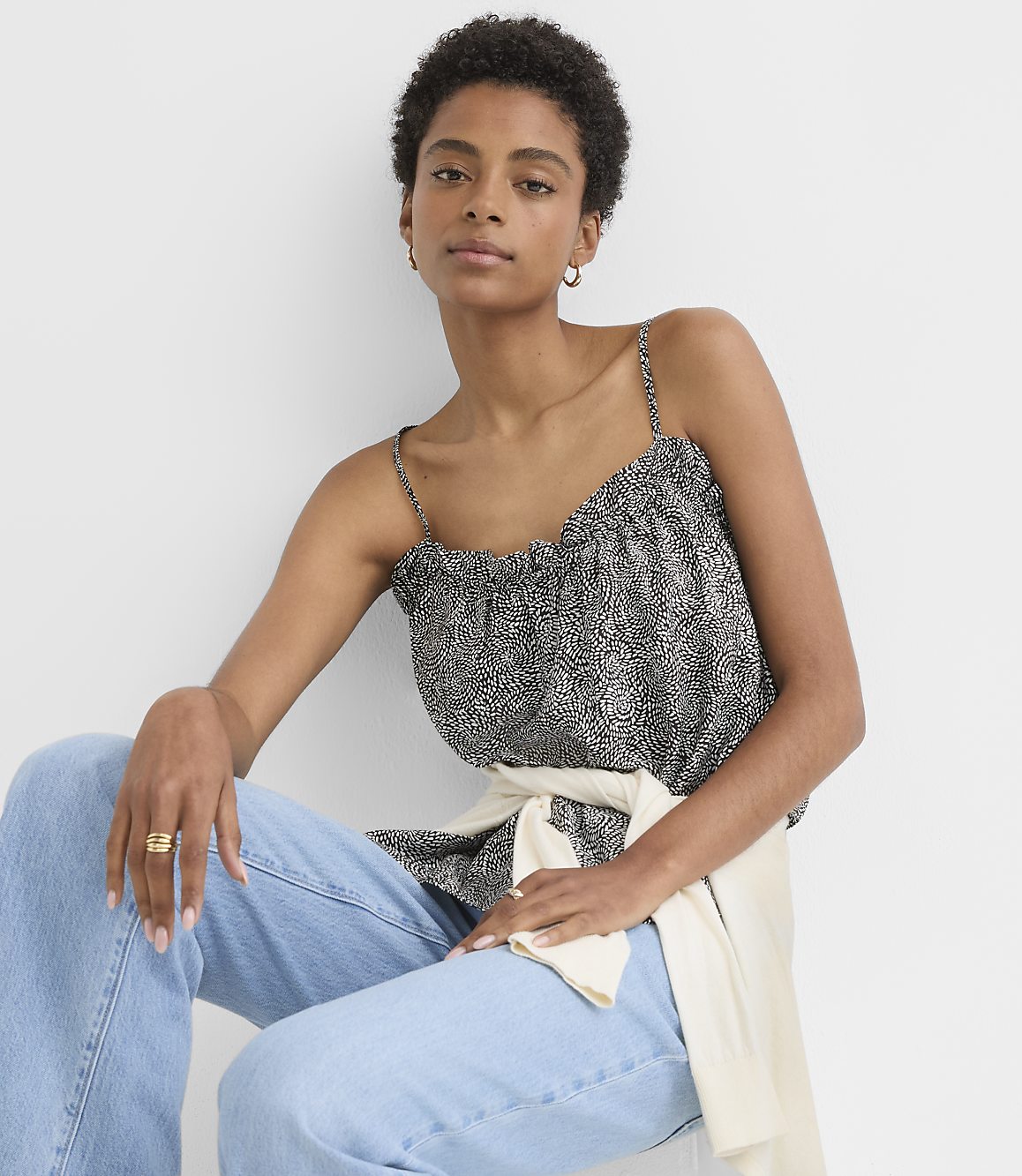 A woman in a patterned camisole and jeans sits against a plain white background.