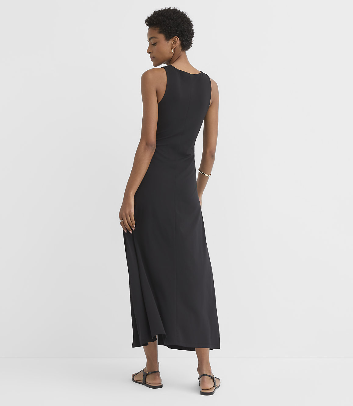 A woman in a black maxi dress stands against a plain white background.