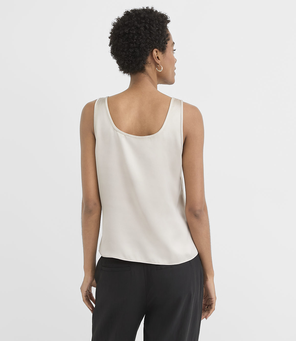 A woman in a light-colored tank top and black pants stands against a plain white background.