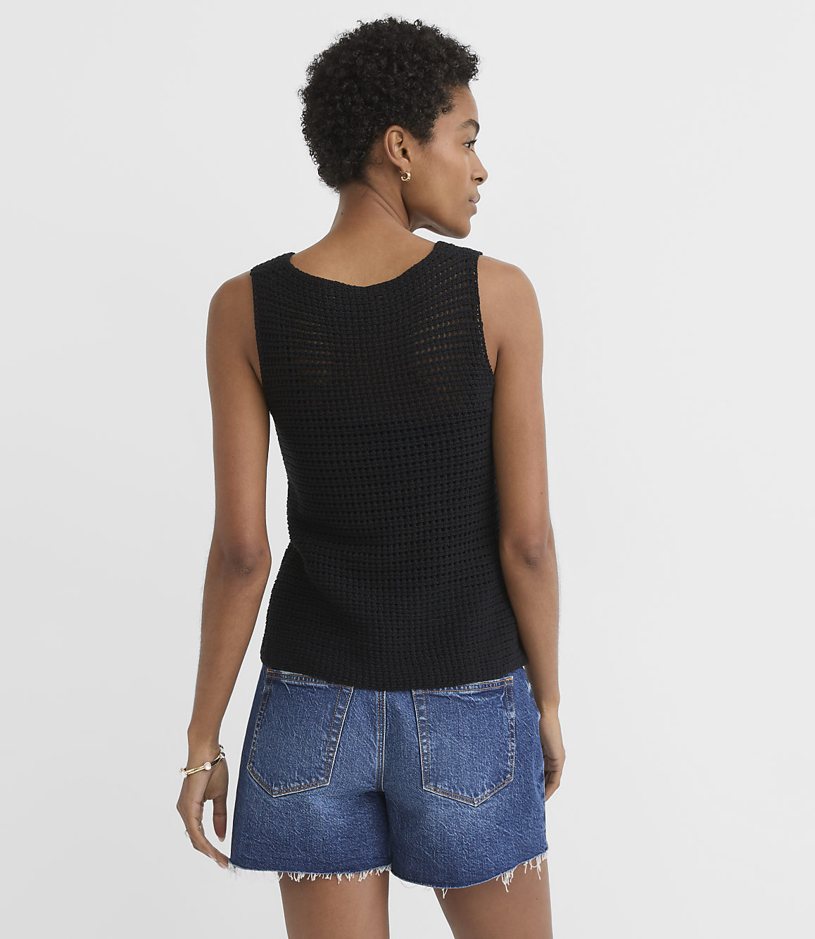 A woman in a black knit tank top and denim shorts stands against a plain white background.