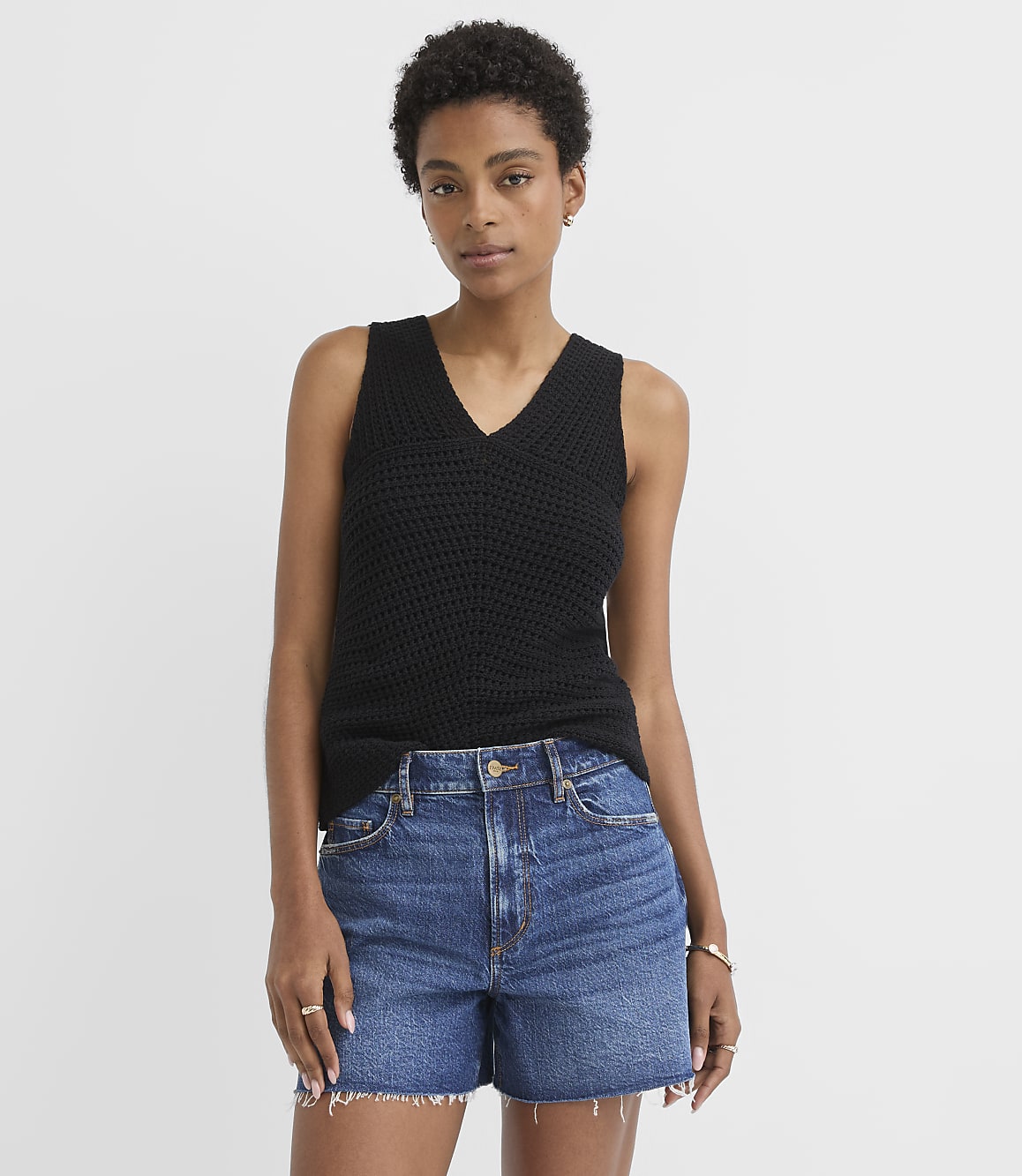 A woman in a black knit tank top and denim shorts stands against a plain white background.