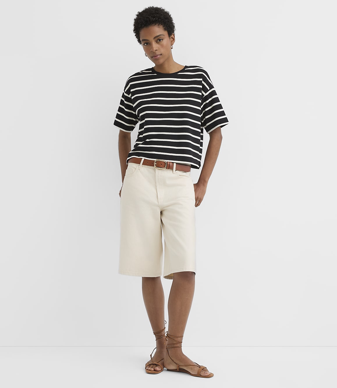 A woman in a striped t-shirt and cream shorts stands against a plain white background.
