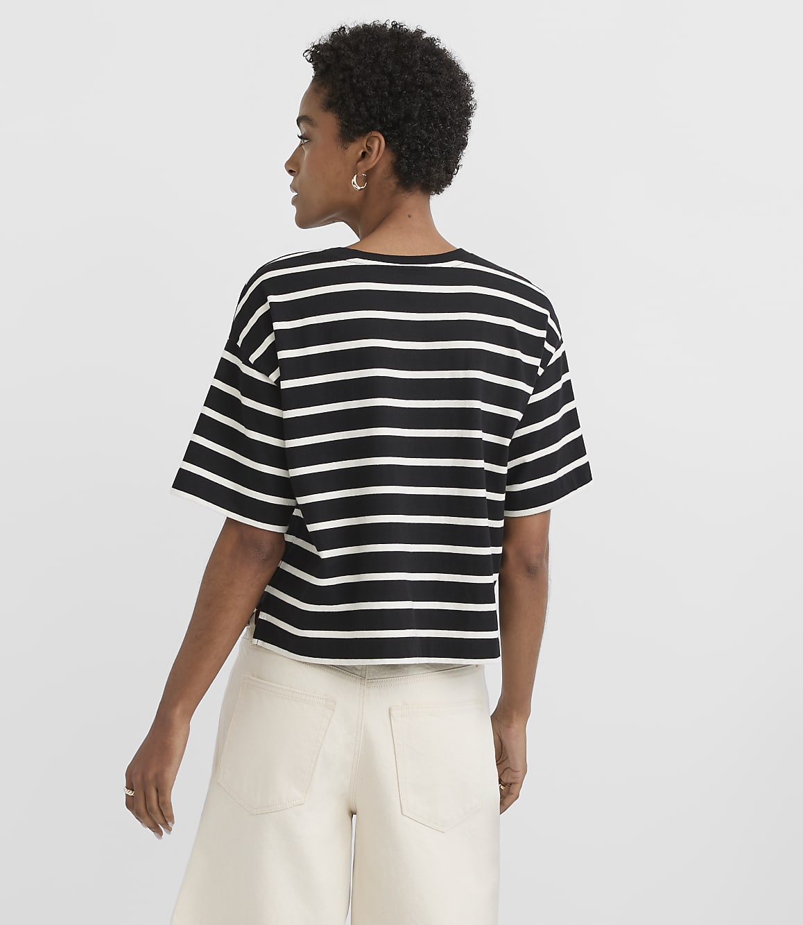 A woman in a striped t-shirt and light-colored pants stands against a plain white background.