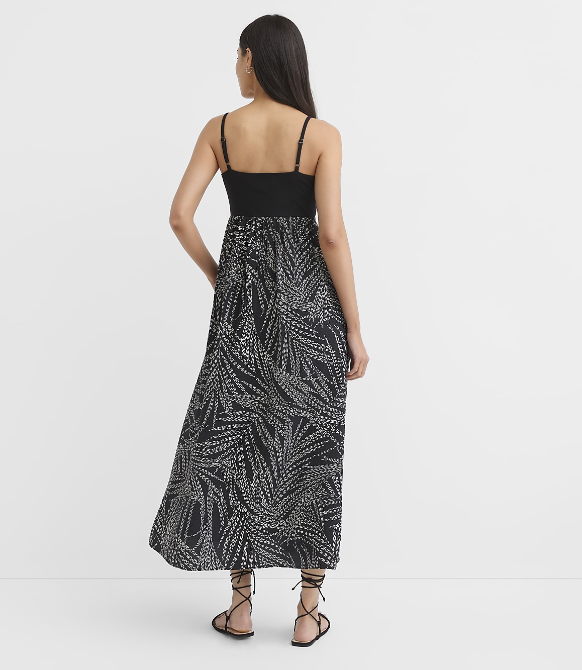 A woman in a black and white patterned maxi dress stands with her back to the camera against a plain white background.
