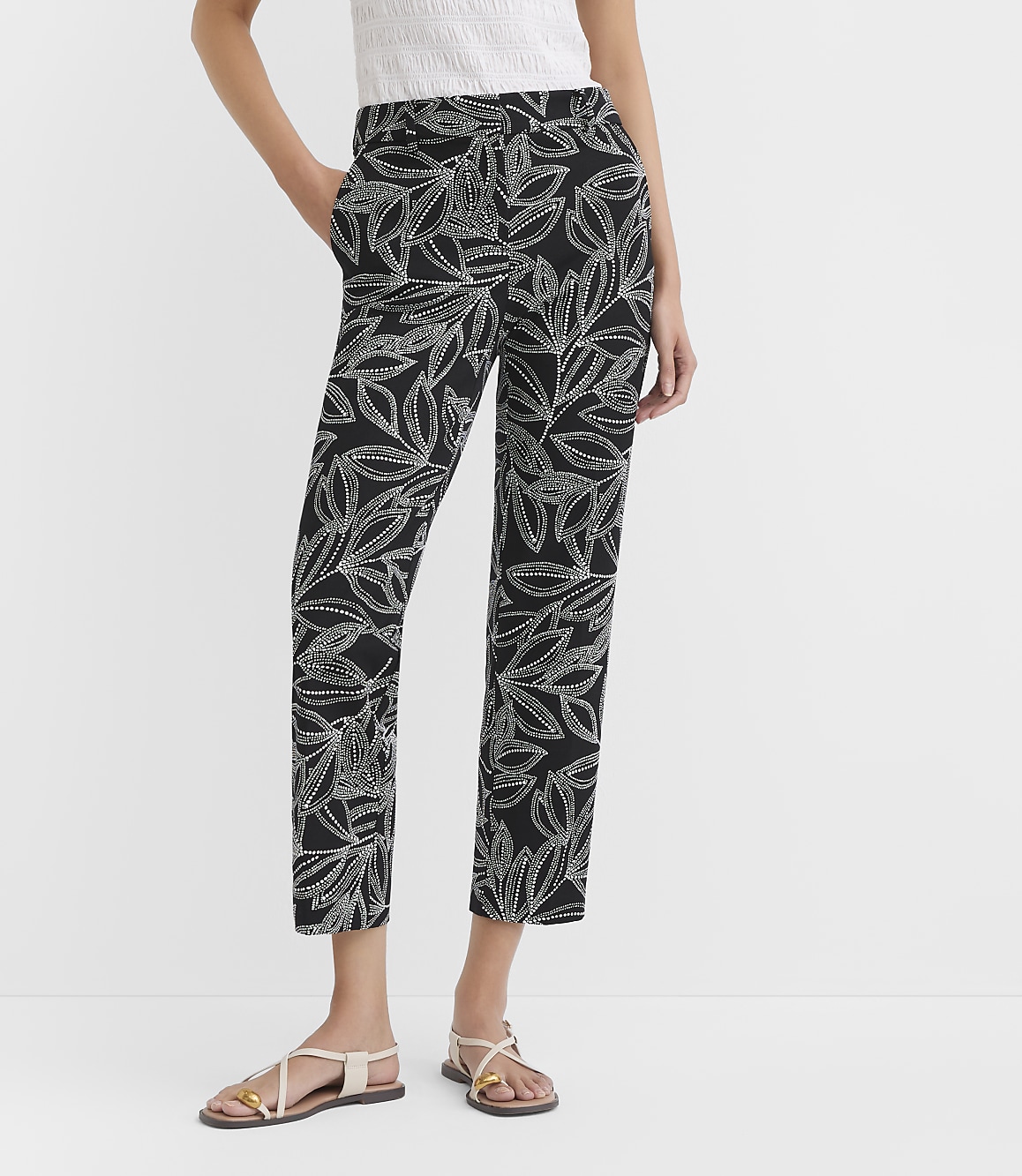 A person models black pants with a white leaf pattern, standing against a plain white background.