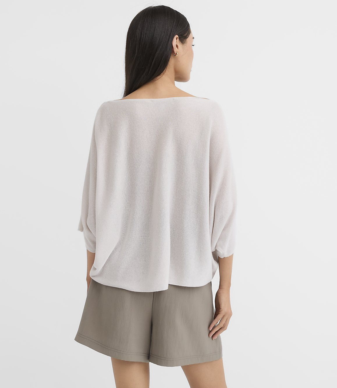 A woman in a light gray sweater and olive shorts stands against a plain white background.