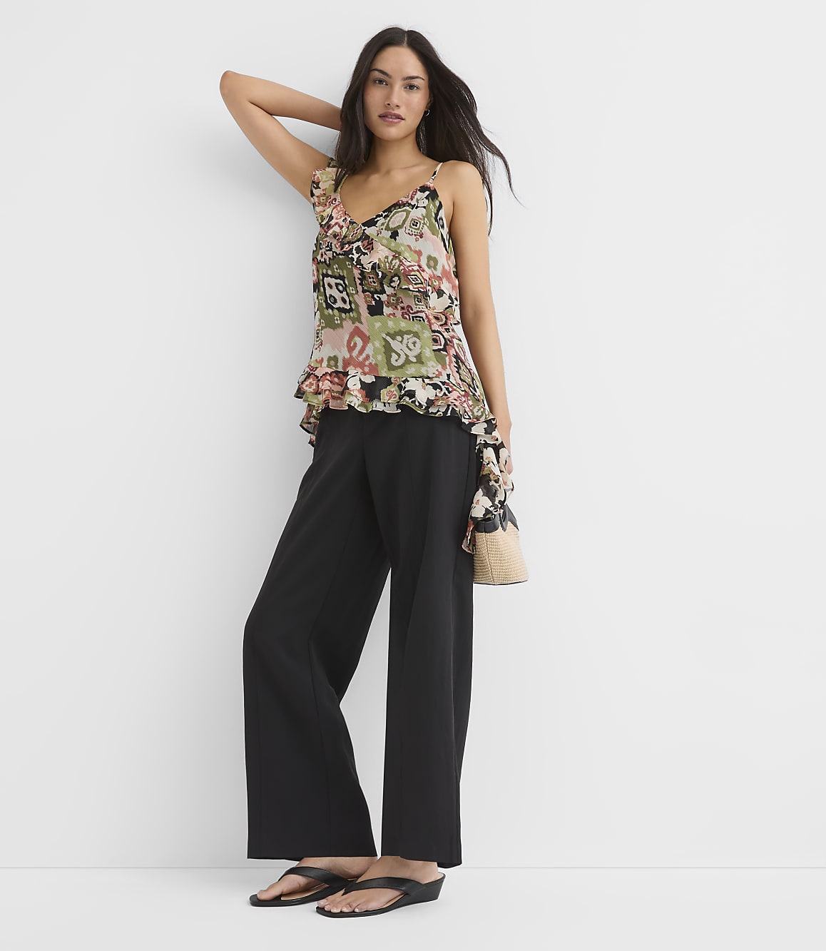 A woman in a floral camisole and black pants poses against a plain white background.