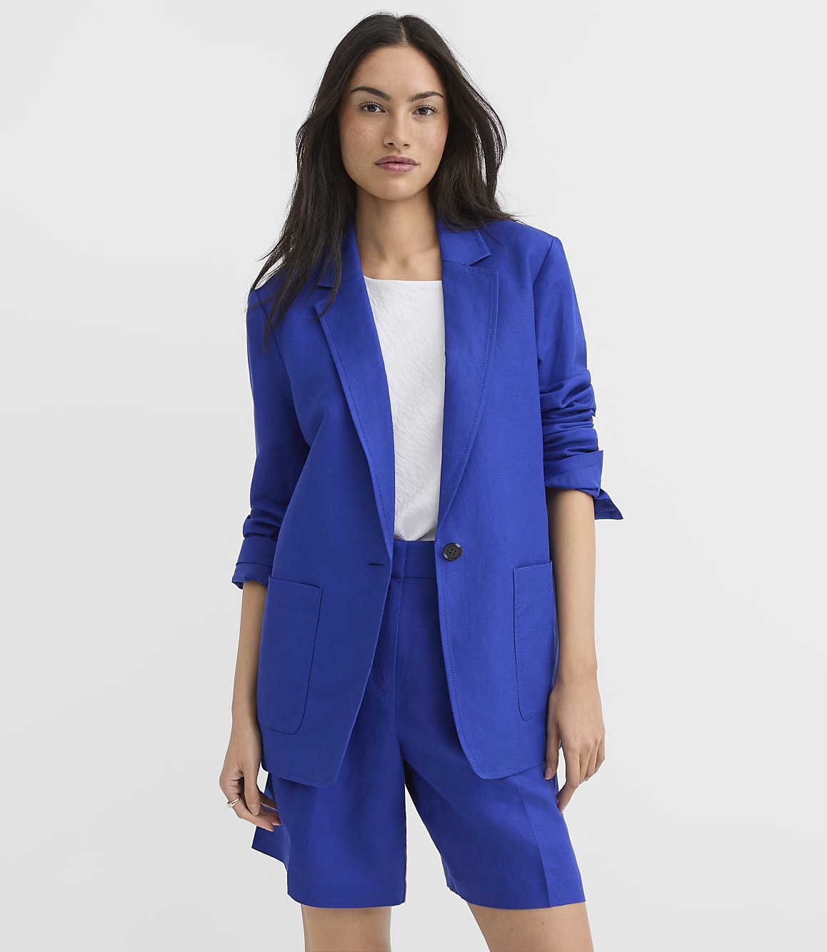 A woman in a blue blazer and shorts stands against a plain white background.