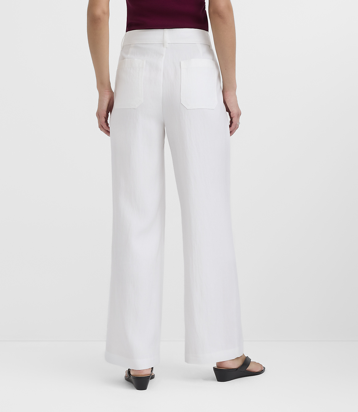 A person wearing white wide-leg pants and black sandals stands against a plain white background.