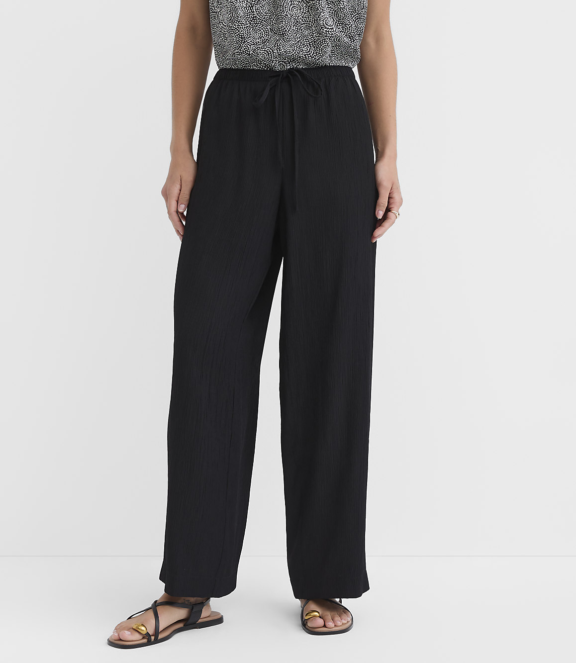 A person stands in black wide-leg pants and sandals against a plain white background.