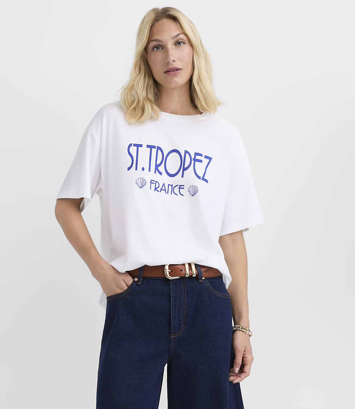 A woman in a white t-shirt with "ST. TROPEZ FRANCE" printed on it stands against a plain white background.