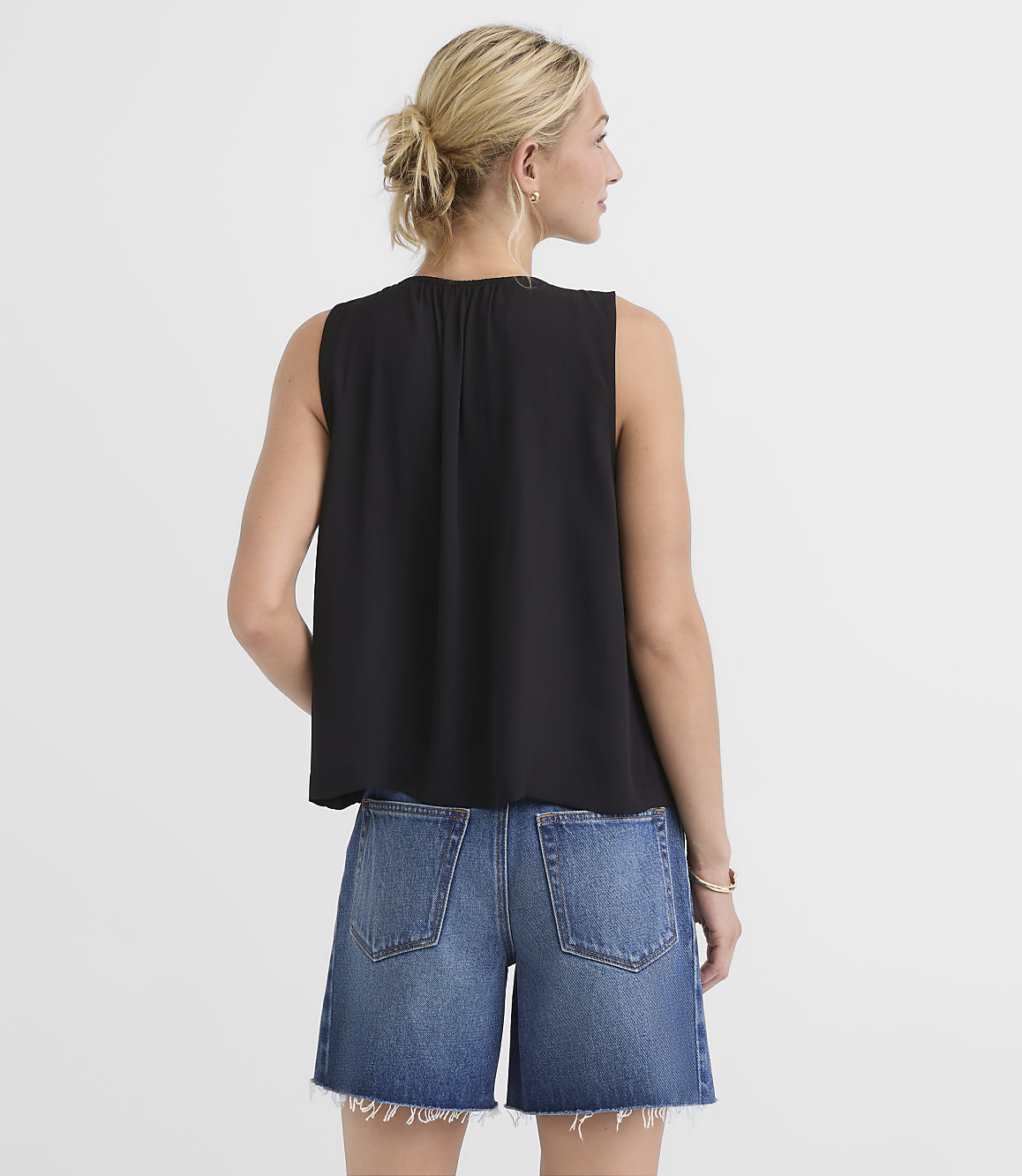 A woman in a black sleeveless top and denim shorts stands against a plain white background.