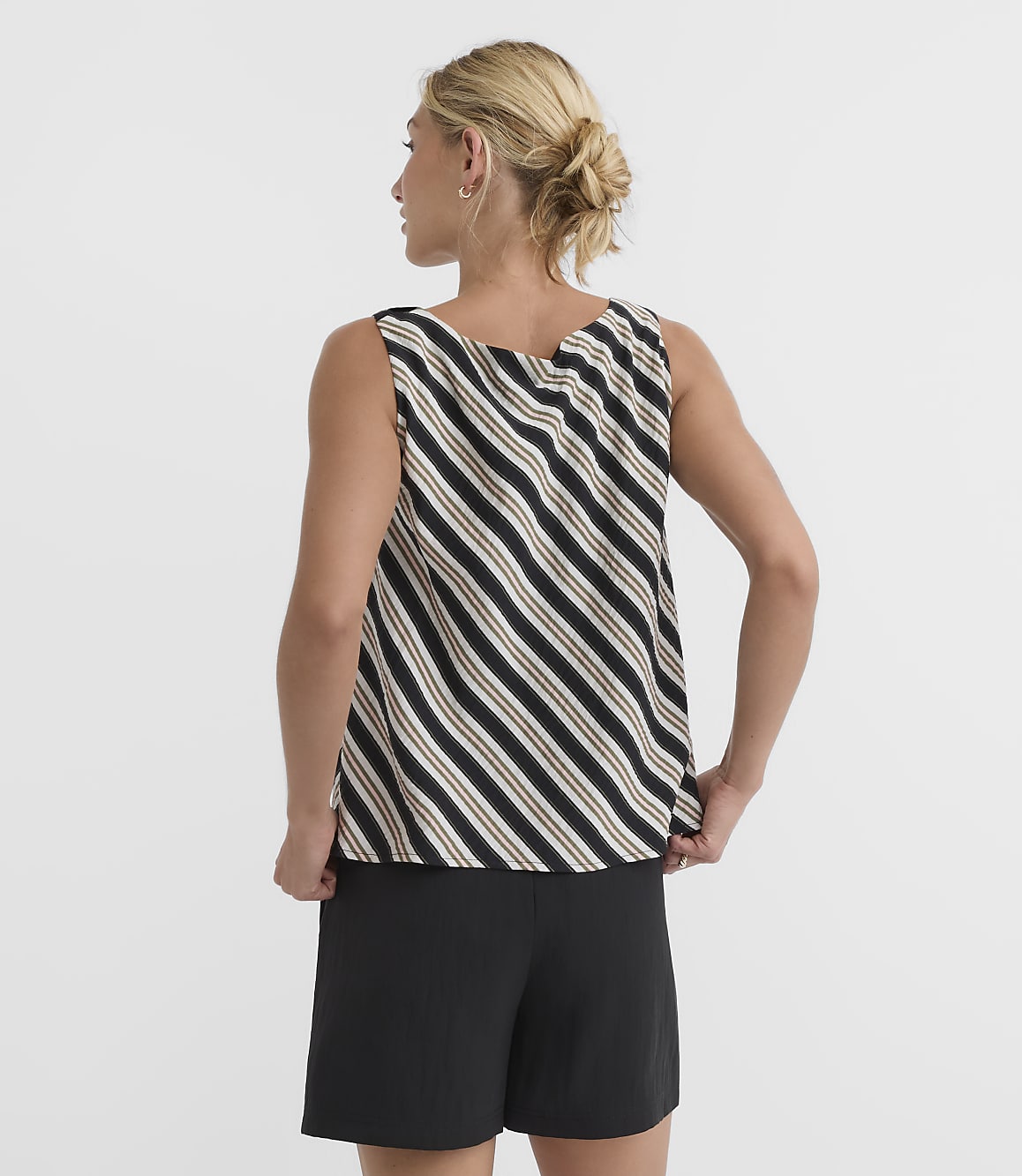A woman in a striped tank top and black shorts stands against a plain white background.