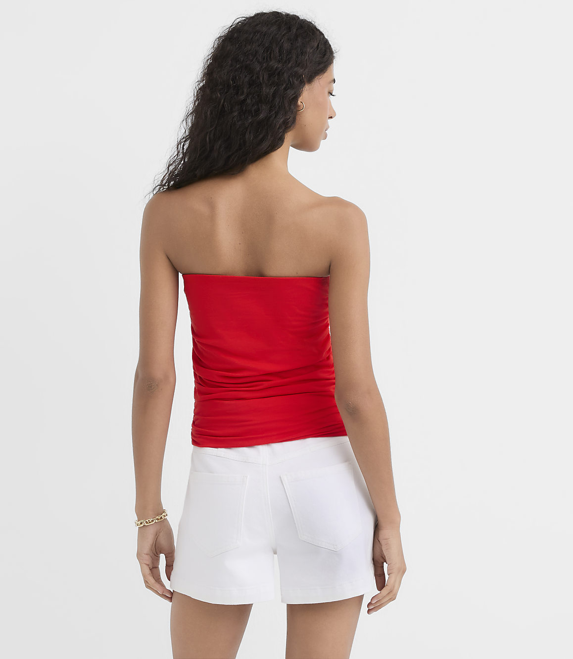 A woman in a red strapless top and white shorts stands against a plain white background.