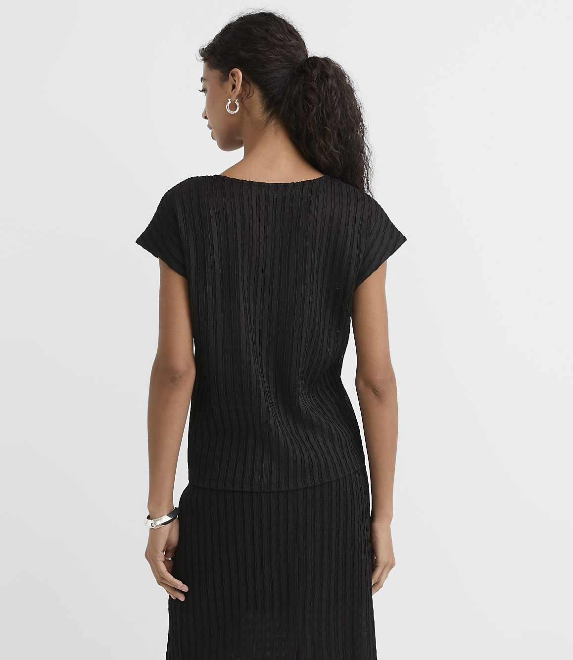 A woman in a black ribbed top and skirt stands against a plain white background.