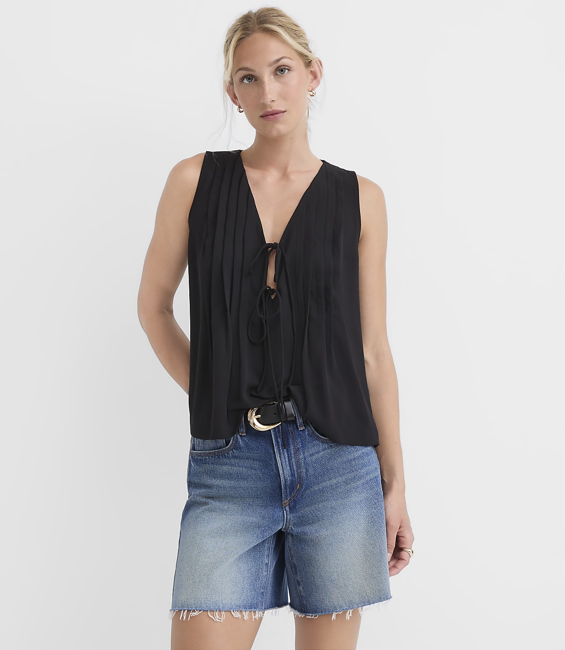 A woman in a black tie-front top and denim shorts stands against a plain white background.