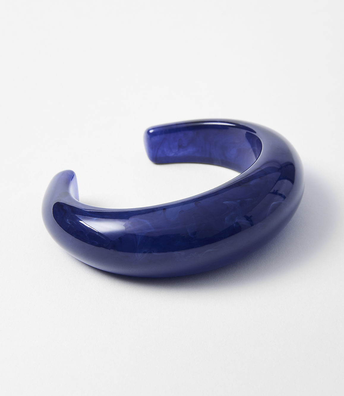 A glossy, deep blue, curved cuff bracelet rests on a plain white background.