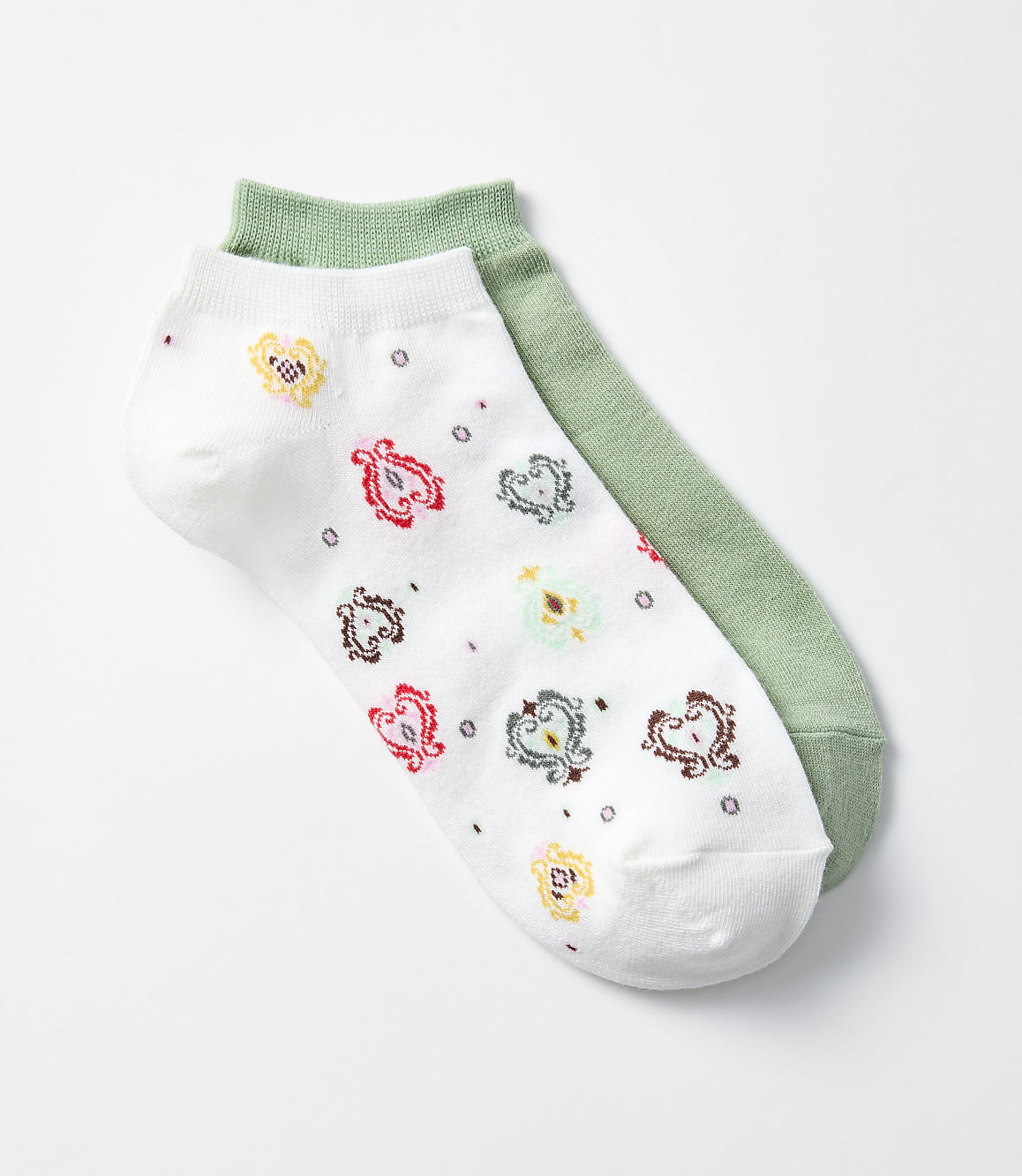 A pair of ankle socks, one white with a colorful paisley pattern and the other solid green, lie on a plain white background.