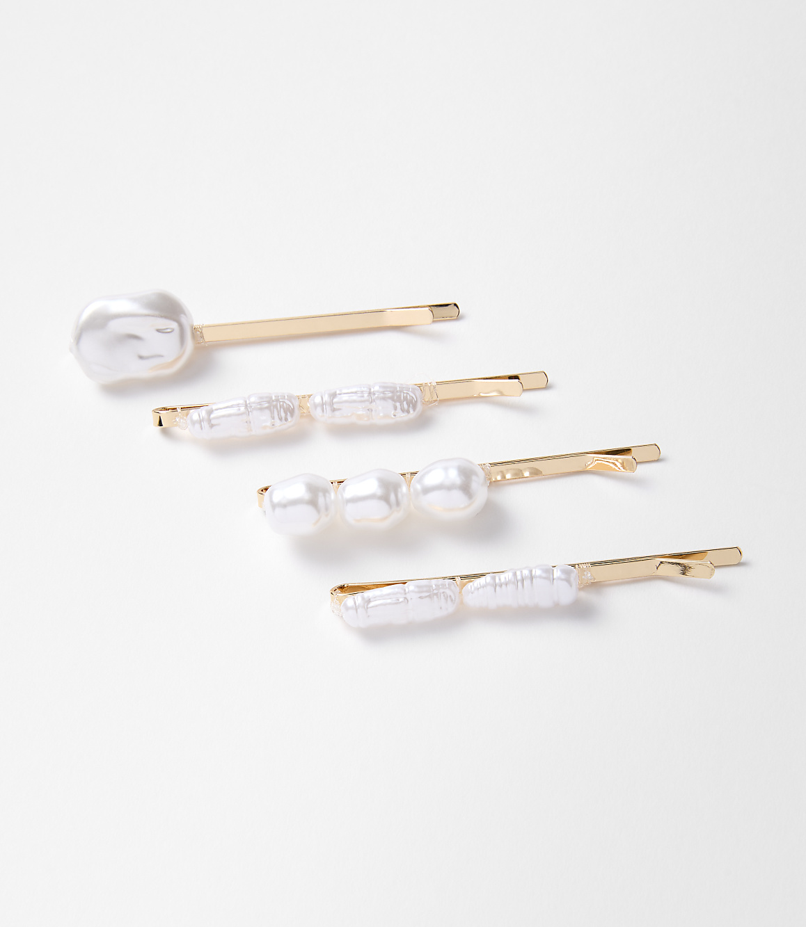 Four gold bobby pins adorned with pearls and pearl-like beads lie on a plain white background.