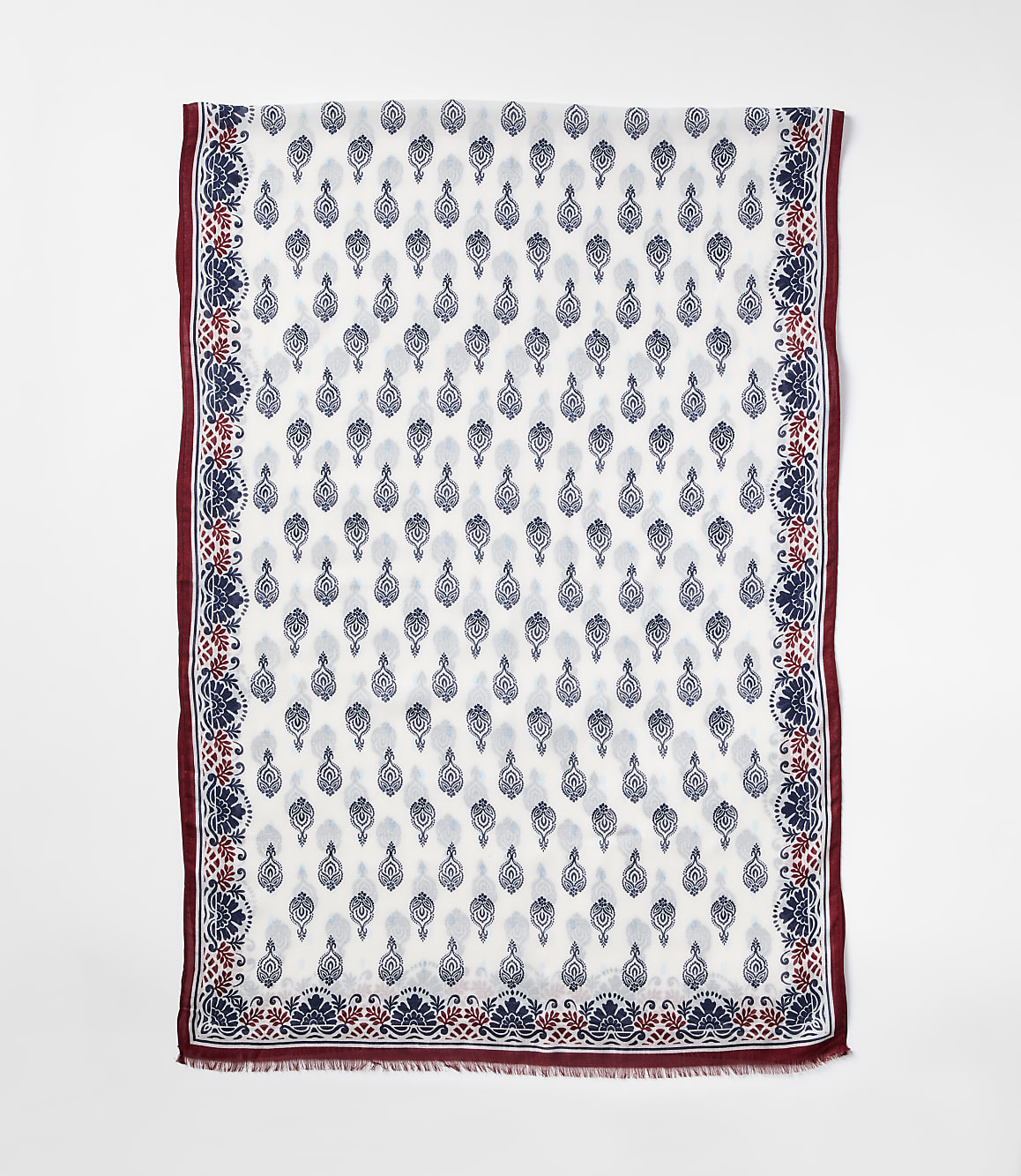 A white scarf with a repeating blue and red floral pattern is laid flat against a plain white background.