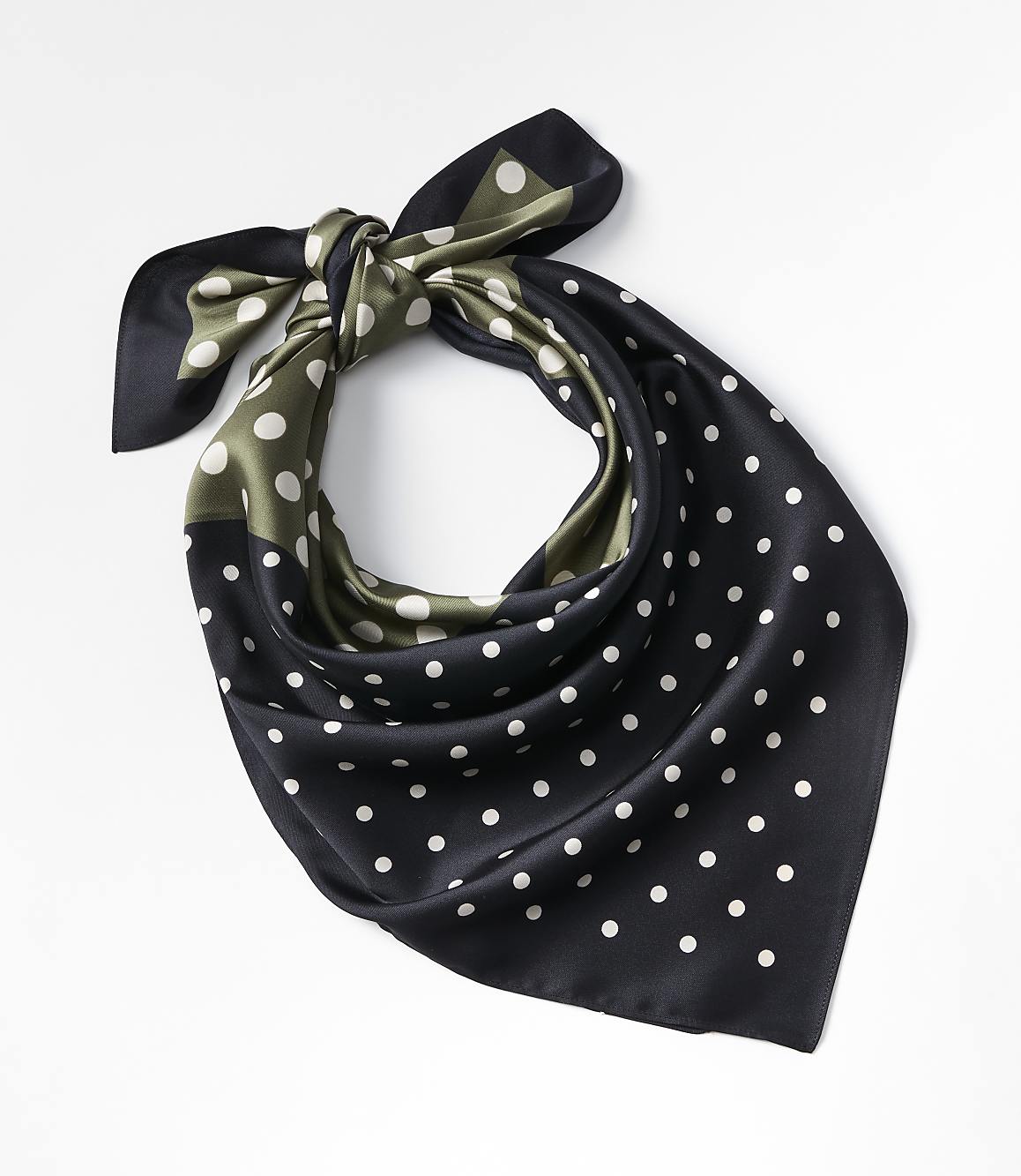 A black and olive green polka dot silk scarf is tied in a knot against a plain white background.