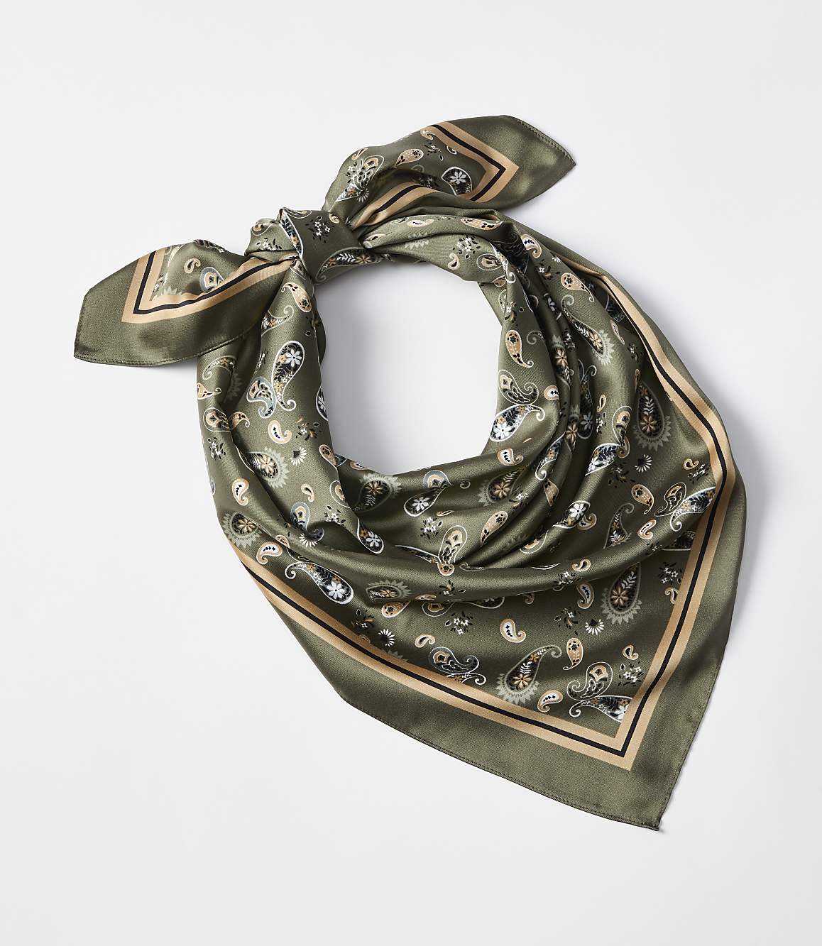 A green paisley-patterned silk scarf is tied in a knot in the foreground against a plain white background.