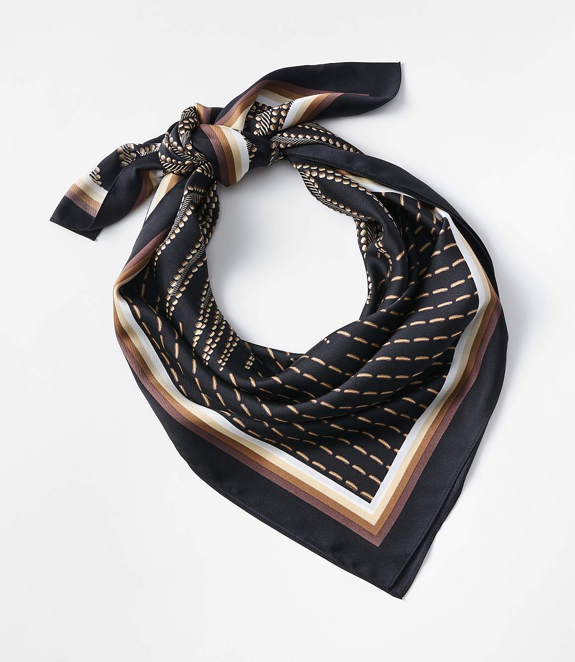 A black silk scarf with a geometric pattern of dots and lines in brown, beige, and white is tied in a knot against a plain white background.