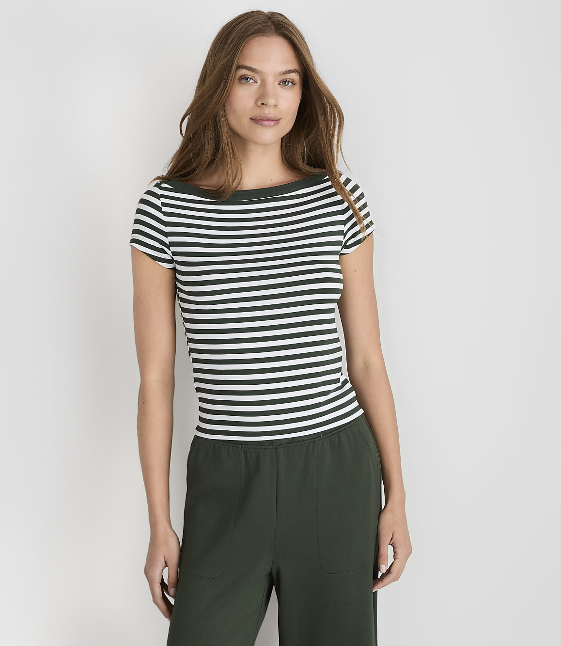 A woman in a striped shirt and green pants stands against a plain white background.