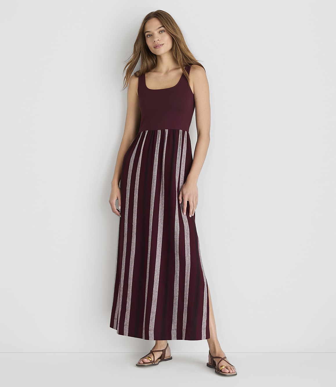 A woman in a burgundy and white striped maxi dress stands against a plain white background.