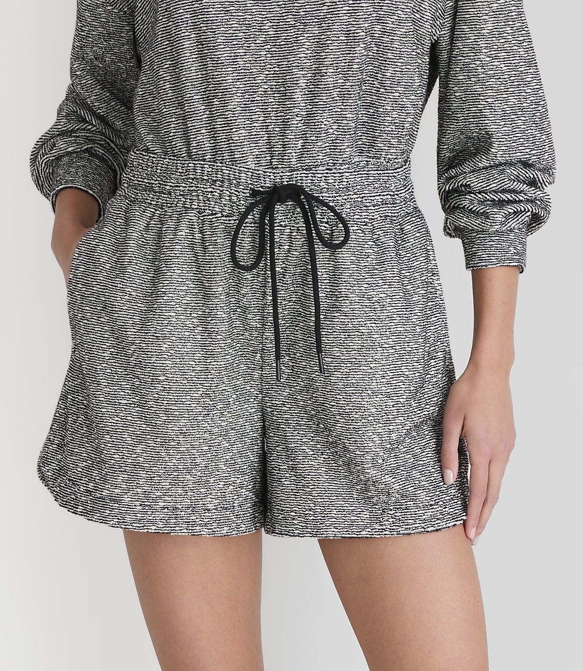 A person models a grey and white patterned romper with a black drawstring in the foreground, against a plain white background.
