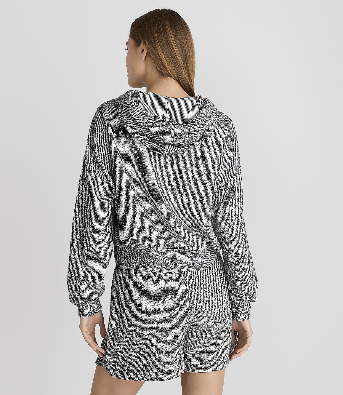 A woman in a sparkly grey hoodie and shorts stands against a plain white background.