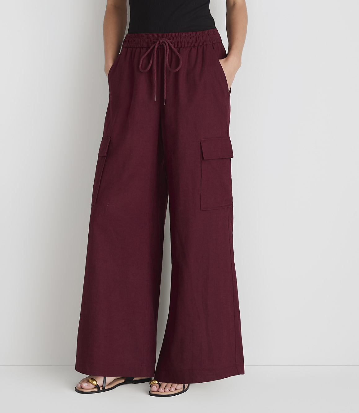A person stands in front of a plain white background, wearing loose-fitting maroon cargo pants with their hands in their pockets.