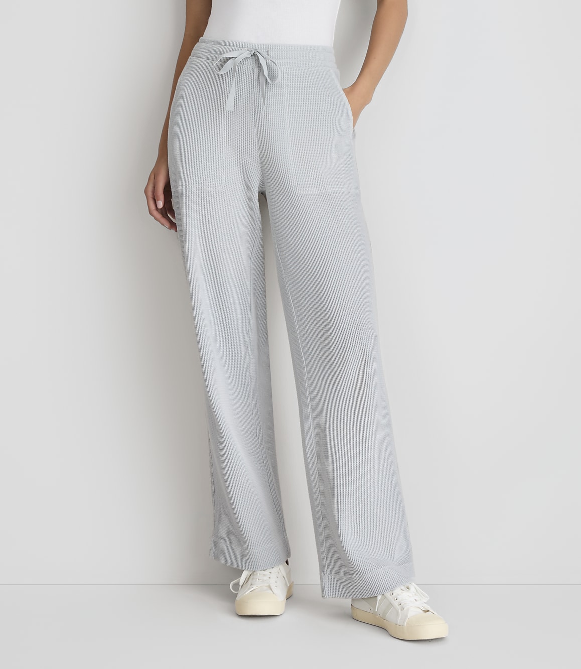 A person stands in light blue, wide-leg, drawstring pants and white sneakers against a plain white background.