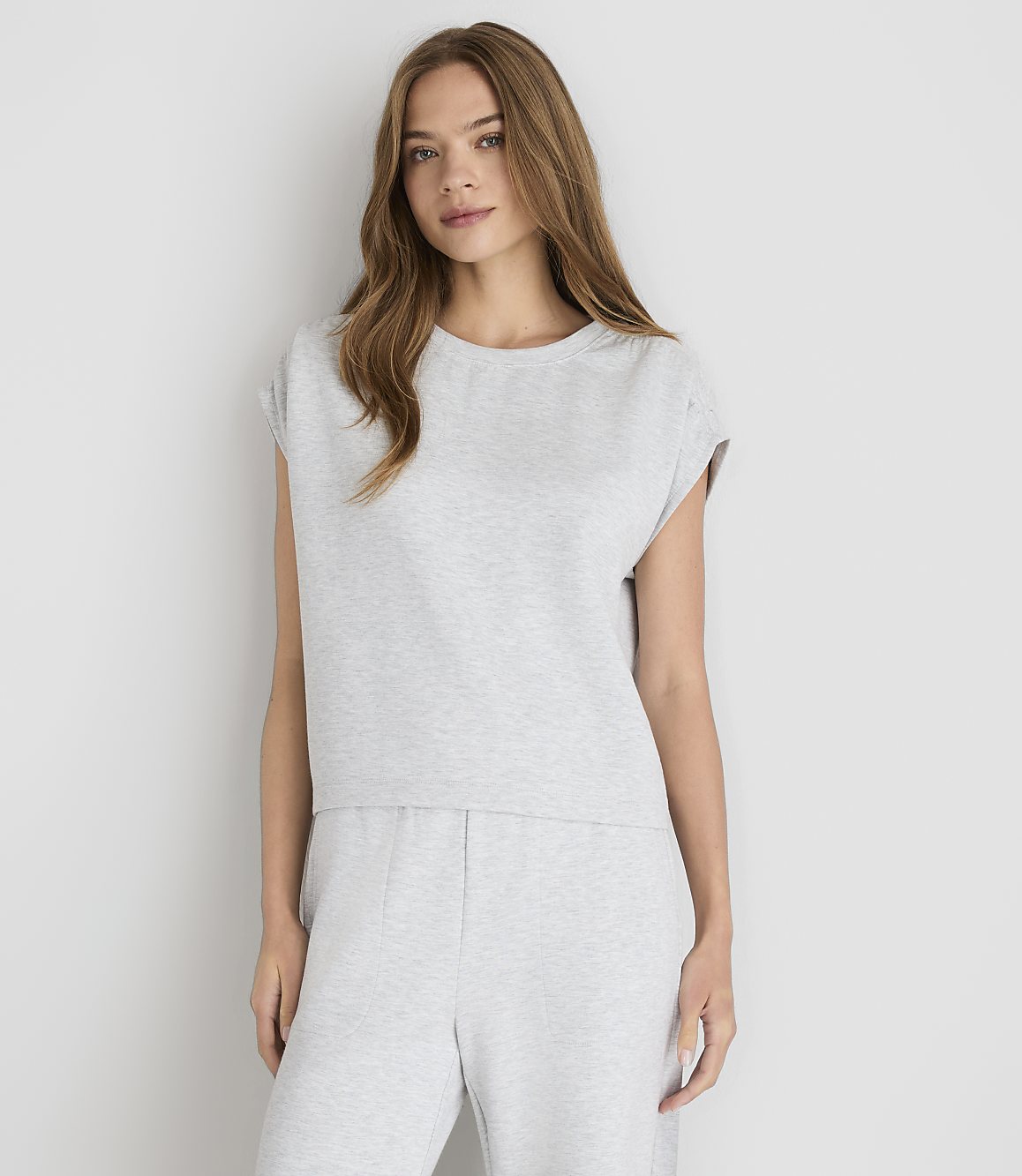 A young woman in a light gray t-shirt and sweatpants stands against a plain white background.