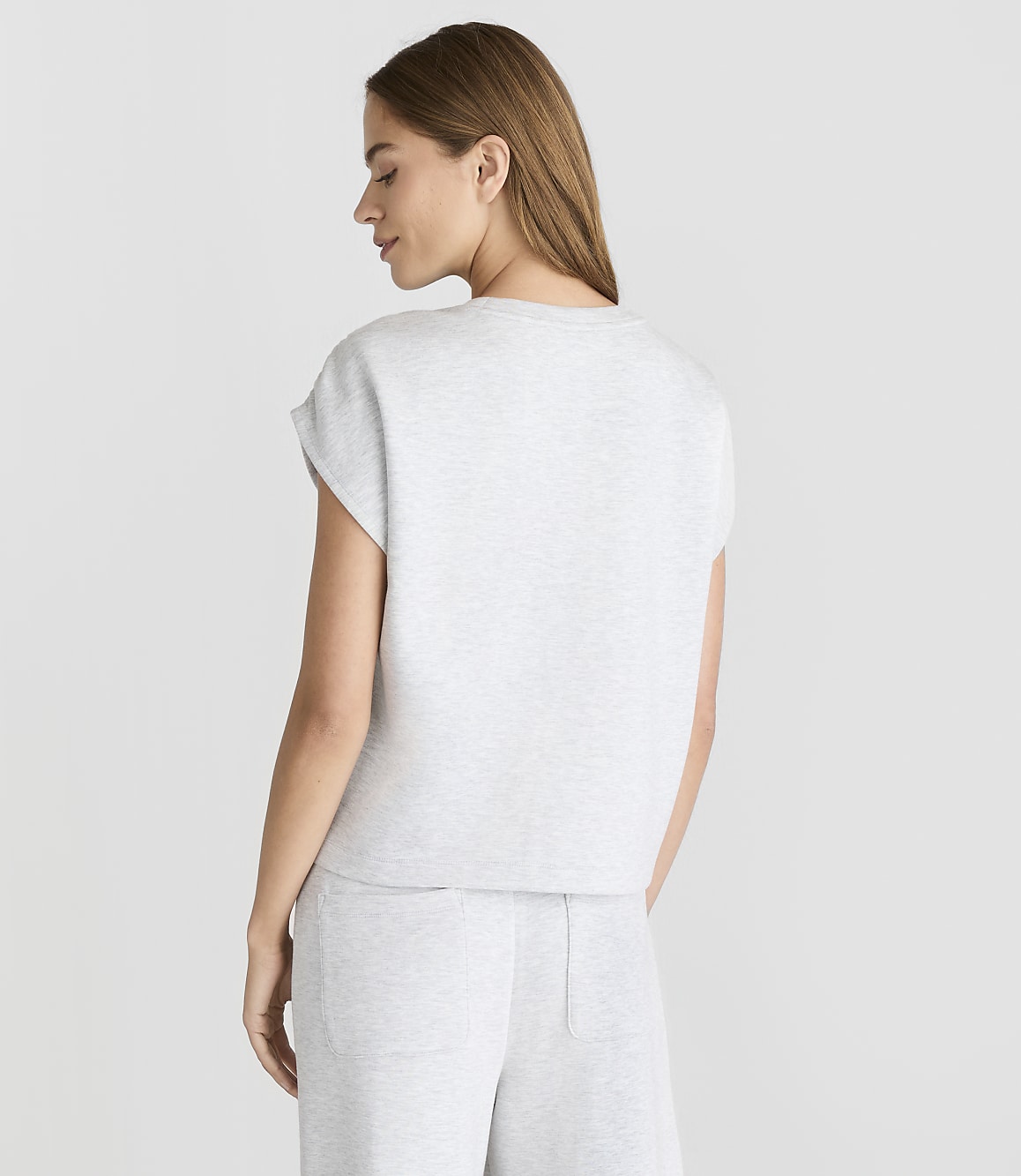 A woman in a light gray t-shirt and pants stands against a plain white background.