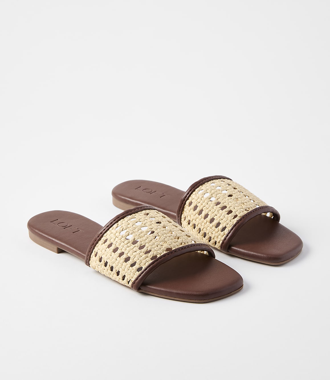 A pair of brown leather slide sandals with woven straw straps rest on a plain white background.
