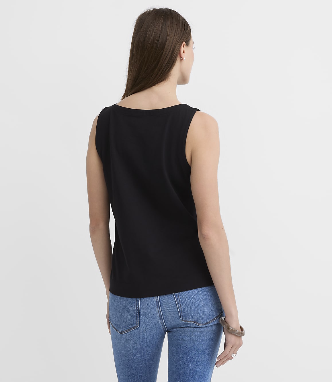 A woman in a black tank top and blue jeans stands against a plain white background.