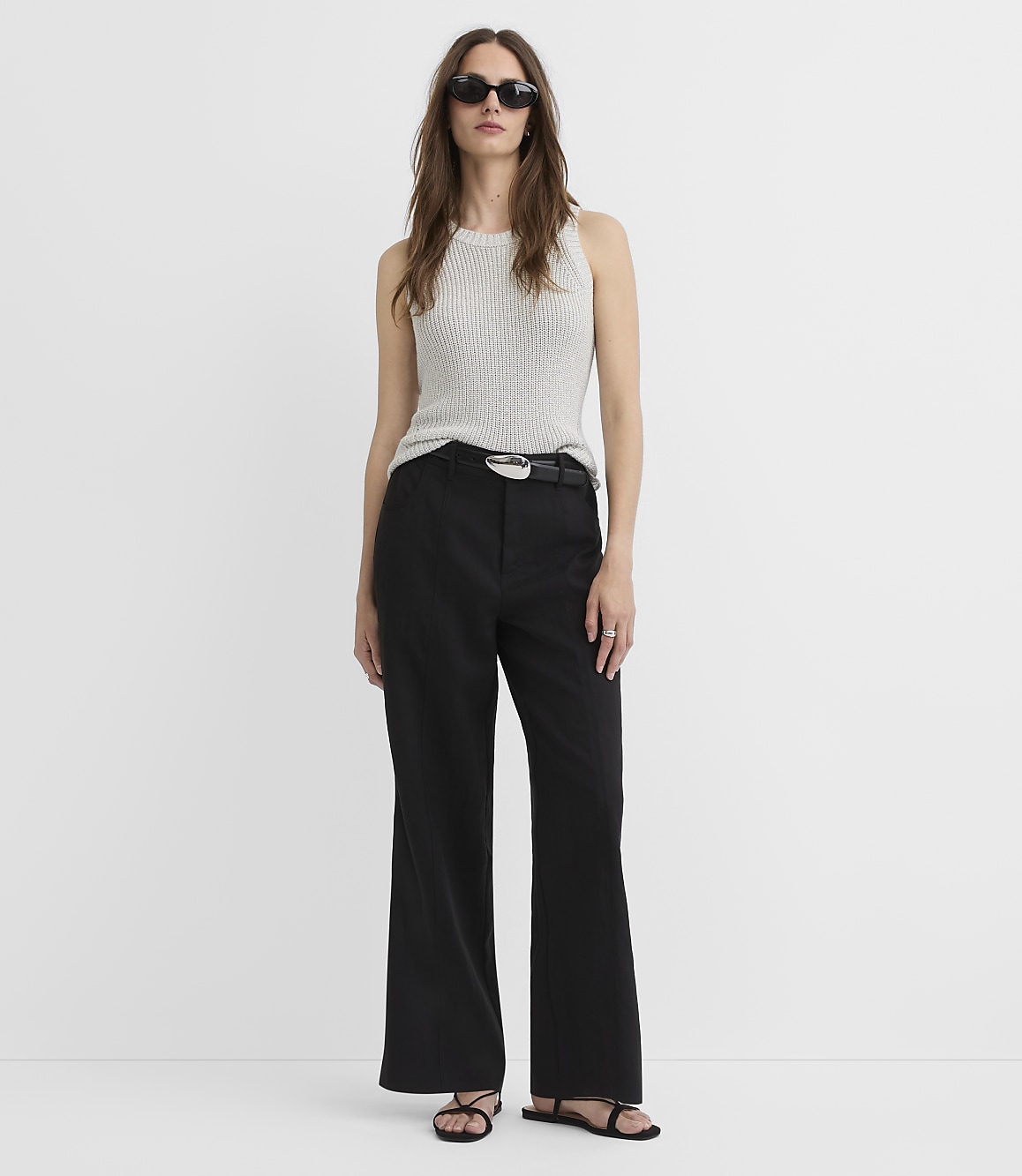 A woman in a white knit top and black wide-leg pants stands against a plain white background.