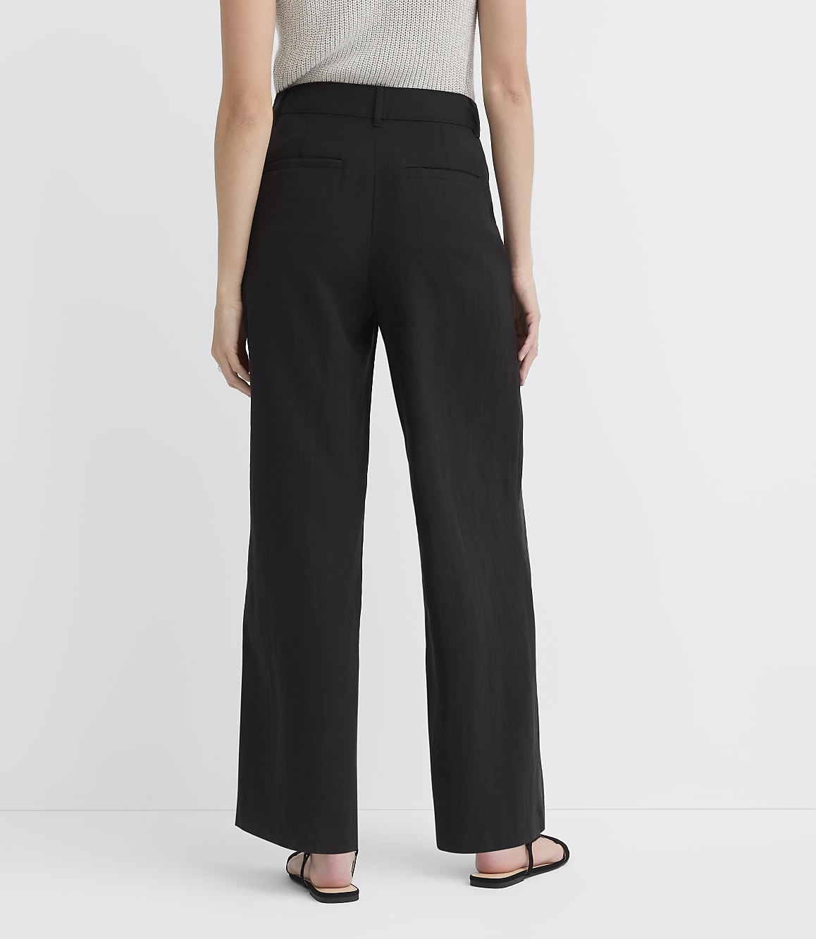 A person wearing black wide-leg pants and sandals stands against a plain white background.