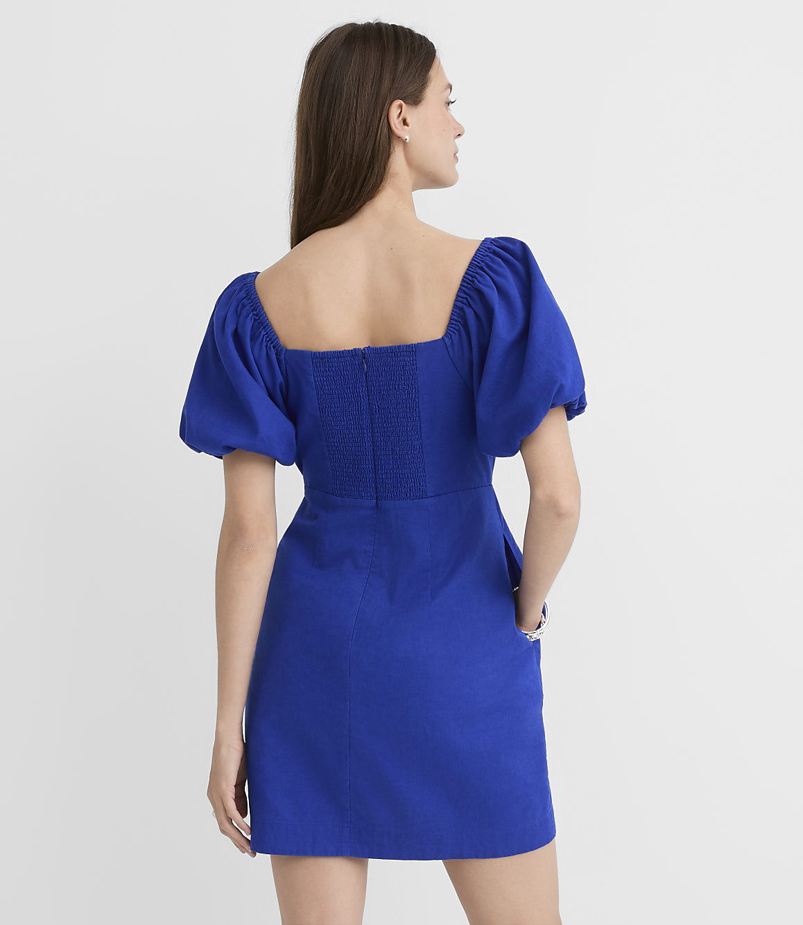 A woman in a blue puff-sleeve dress stands against a plain white background.
