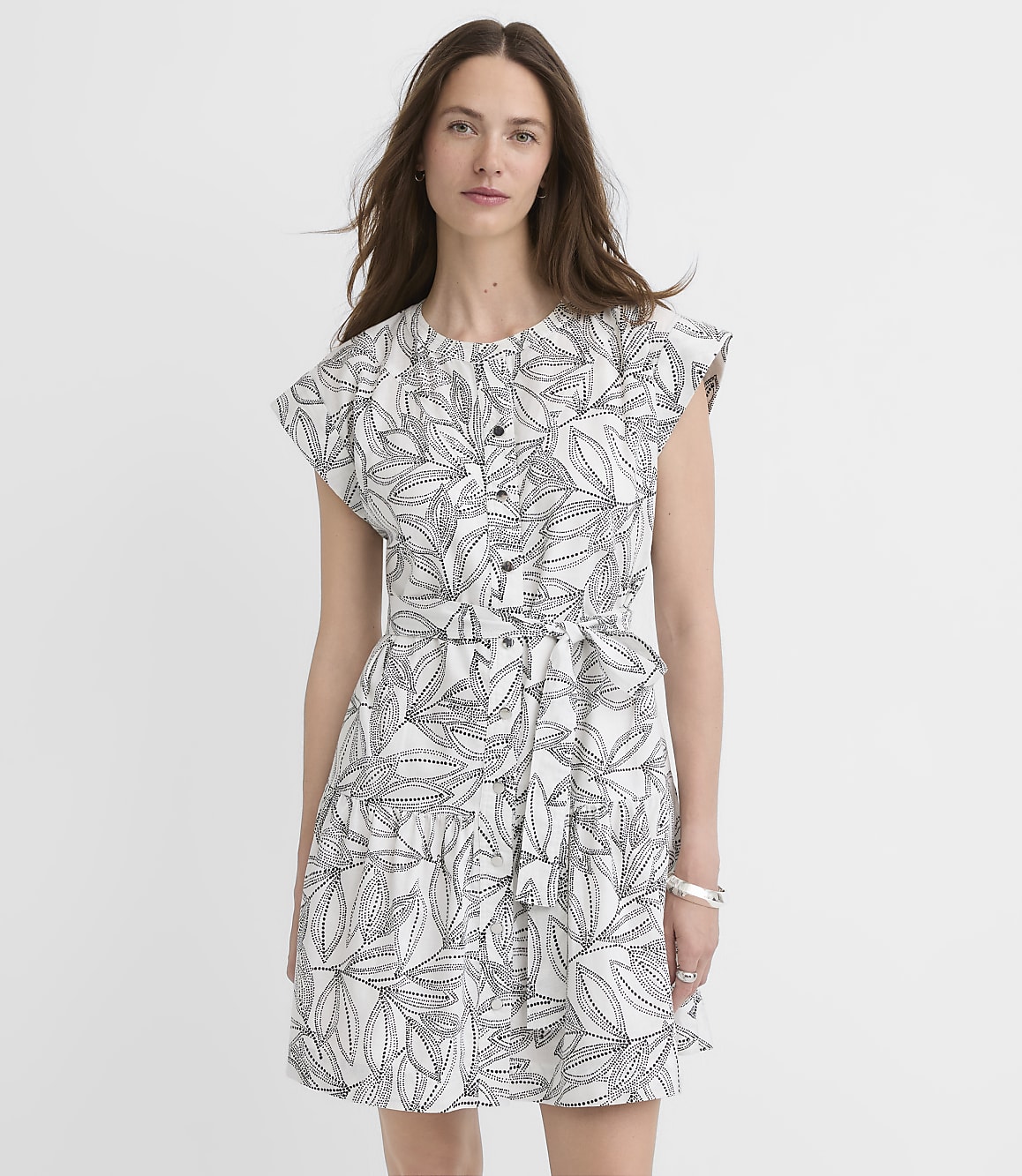 A woman in a white dress with a black leaf print stands against a plain white background.