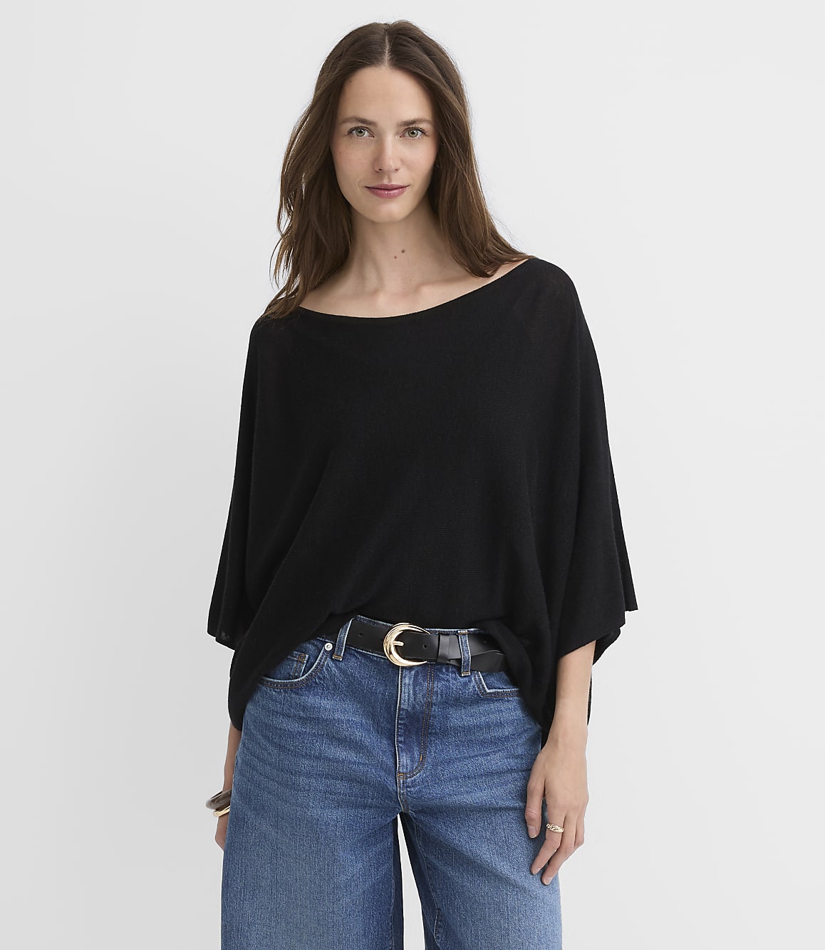 A woman in a black top and blue jeans stands against a plain white background.