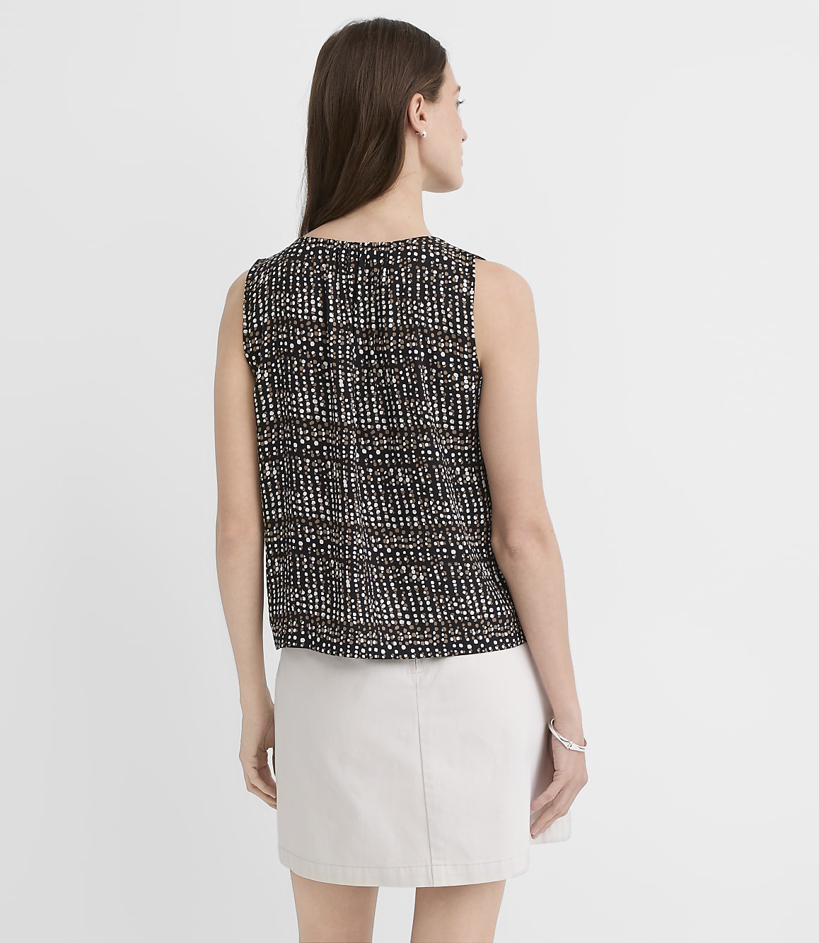 A woman in a patterned sleeveless top and a light-colored skirt stands against a plain white background.