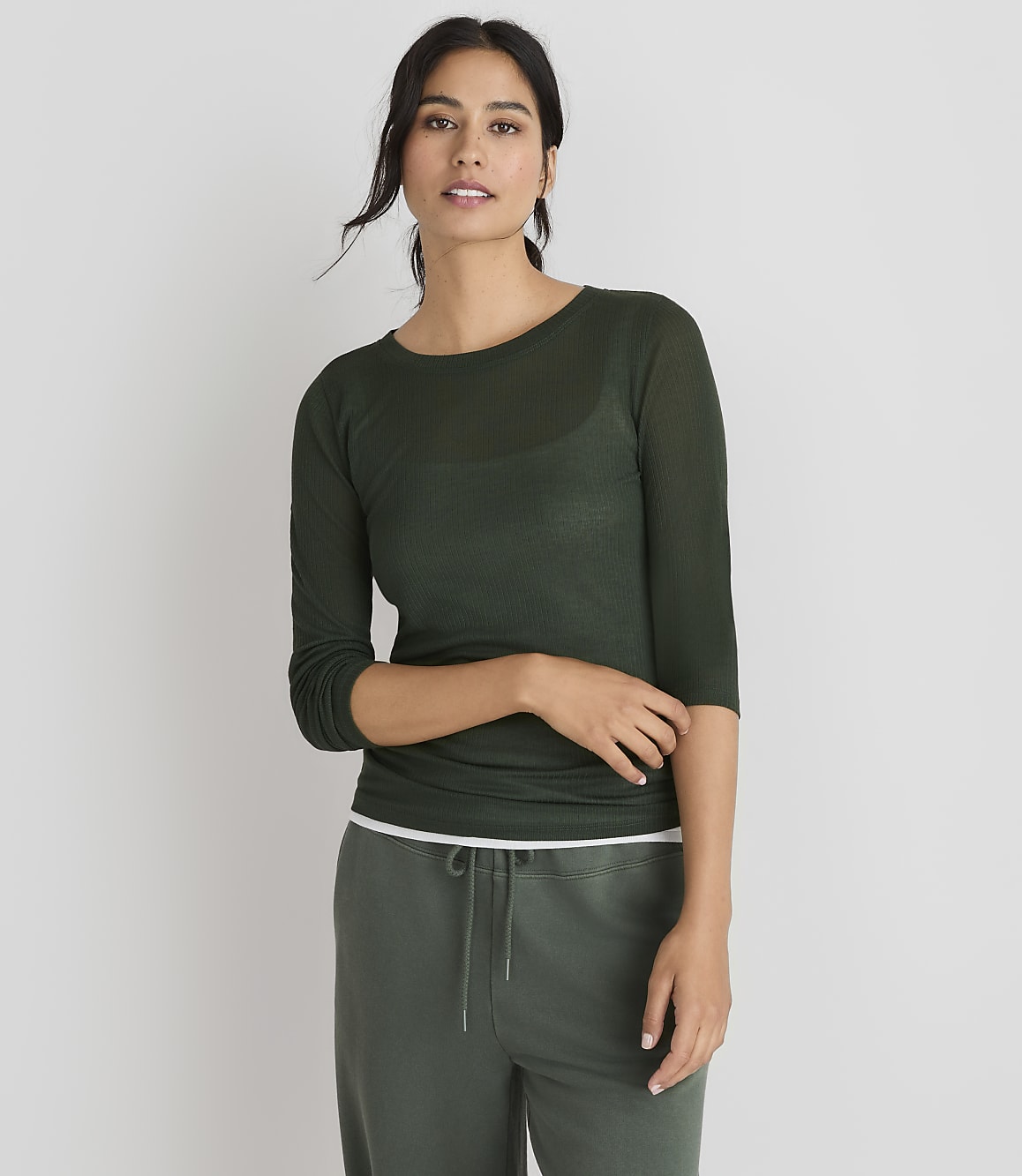 A woman in a green sweater and pants stands against a plain gray background.