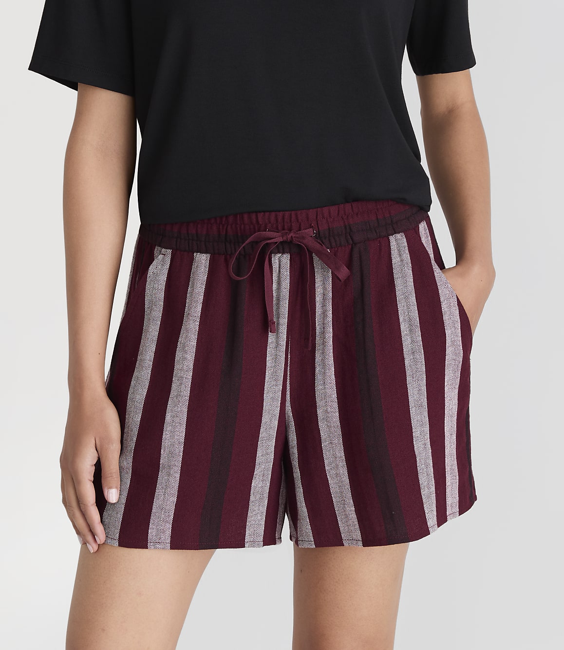 A person in a black t-shirt and striped burgundy shorts stands against a plain white background.